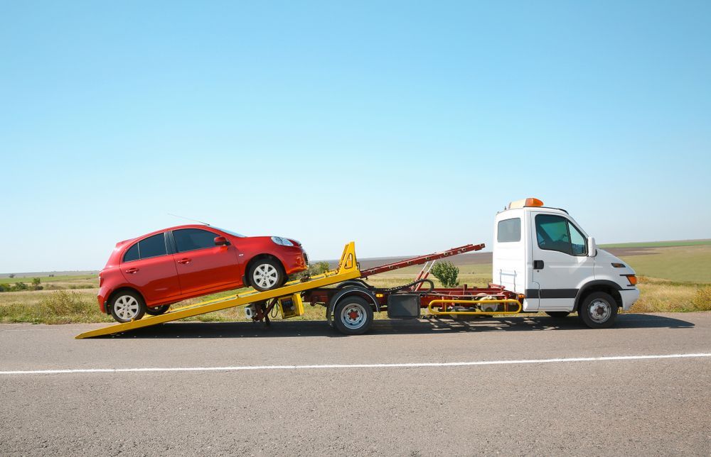Red Car Being Towed by A White Tow Truck on A Road, Under a Blue Sky — Cam Duffy Autos In Ravenshoe, QLD