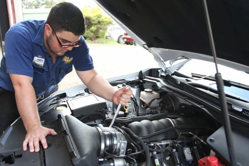 A Man In A Blue Shirt Is Working On The Engine Of A Car — Cam Duffy Autos In Tolga, QLD