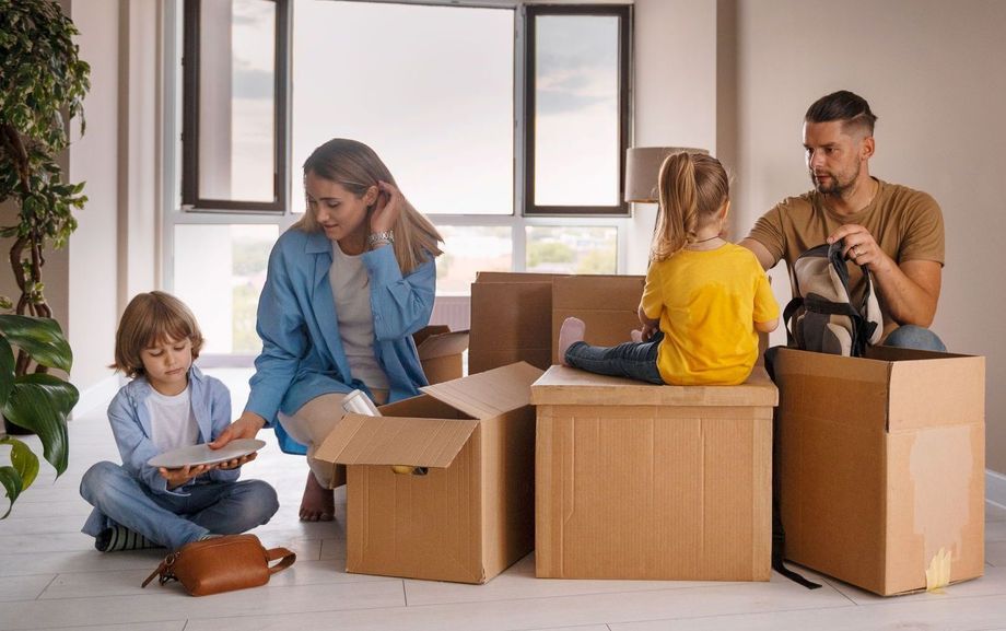 A family is moving into a new home and sitting on cardboard boxes.