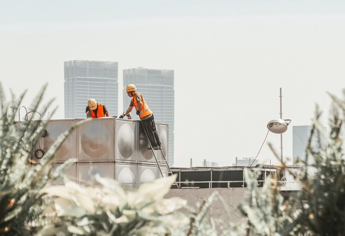 Two construction workers are working on a tank on top of a building.