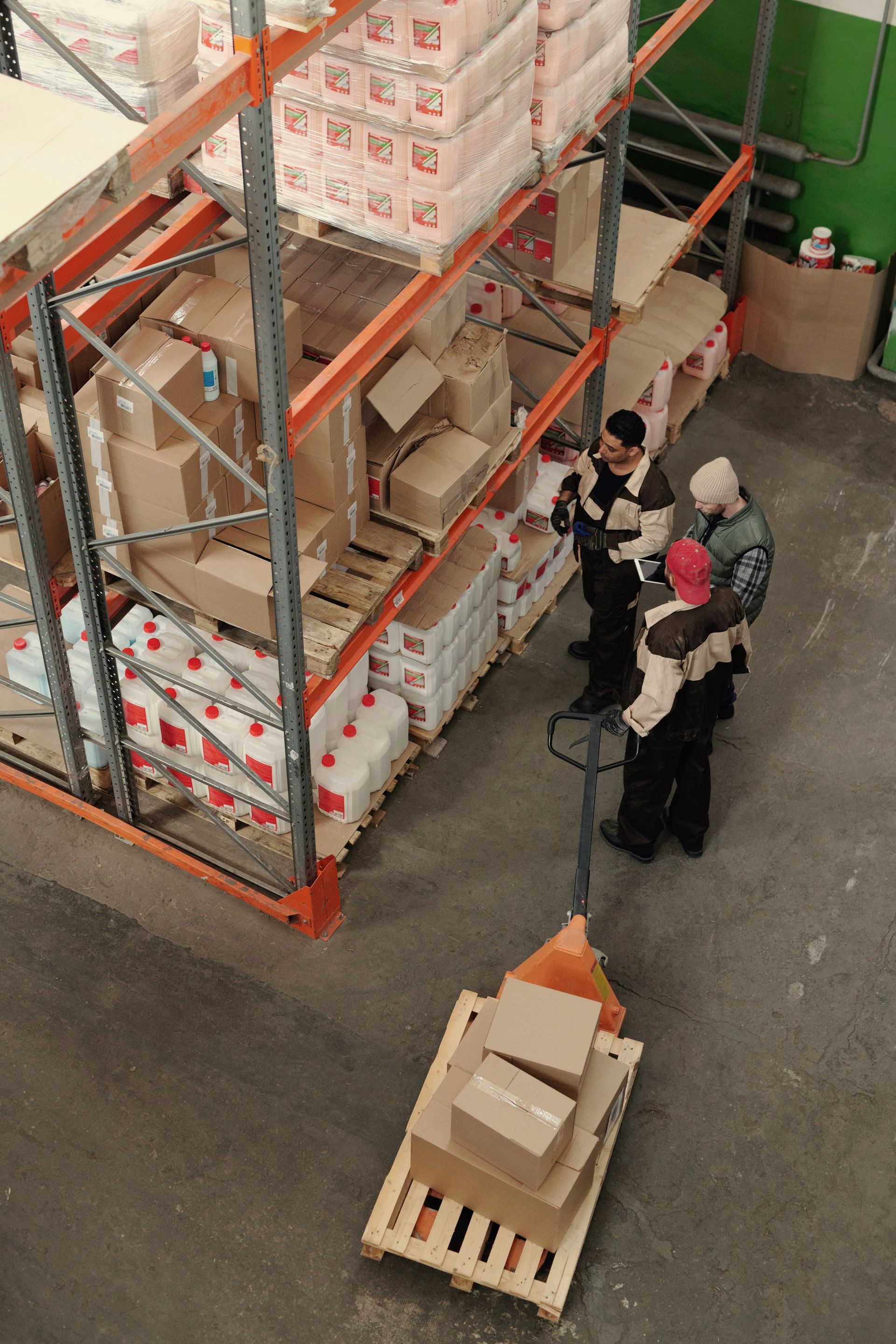 A group of people are standing around a pallet in a warehouse.