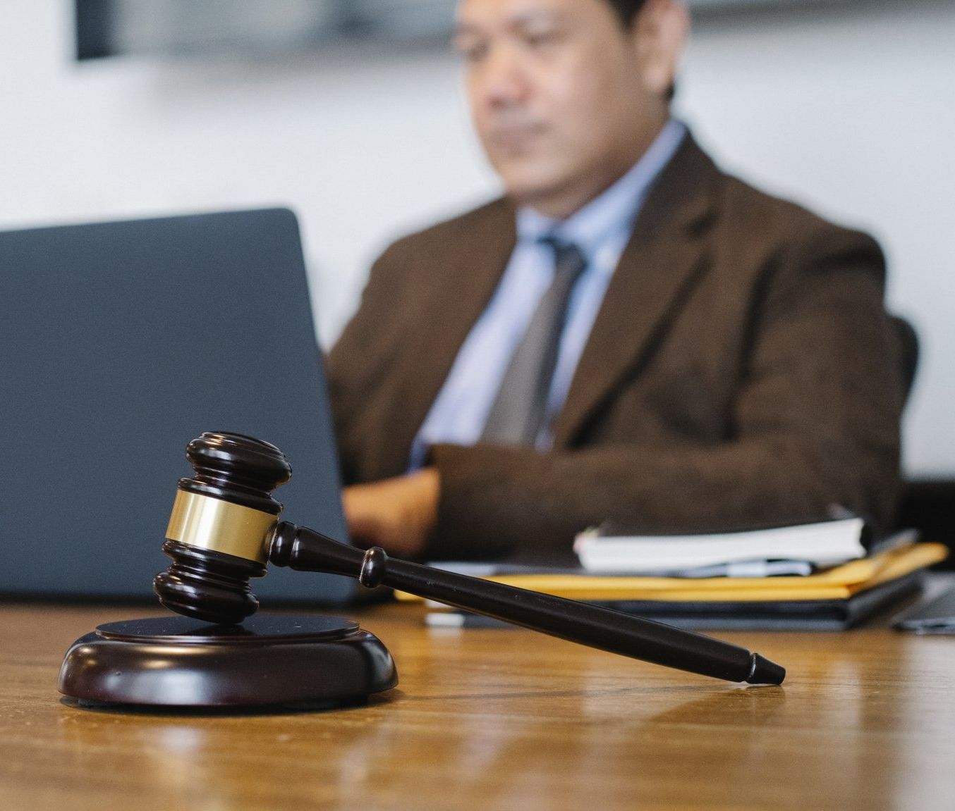 A judge 's gavel is sitting on a wooden table in front of a man using a laptop.