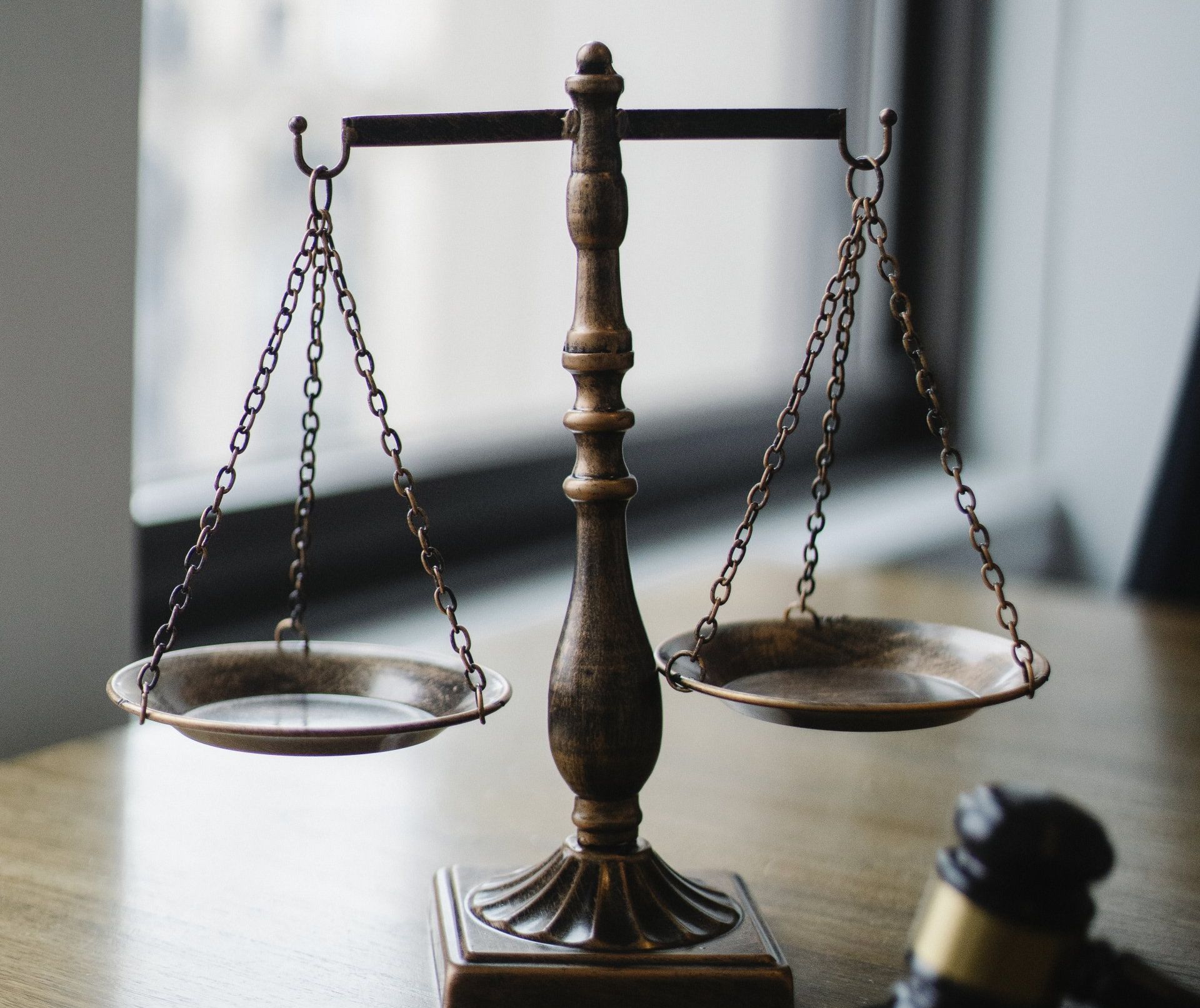 A scale of justice is sitting on a wooden table next to a gavel.