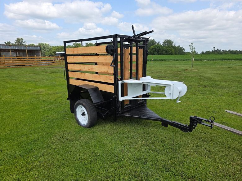 Black utility trailer with wooden slats and hitch parked on grass in a field