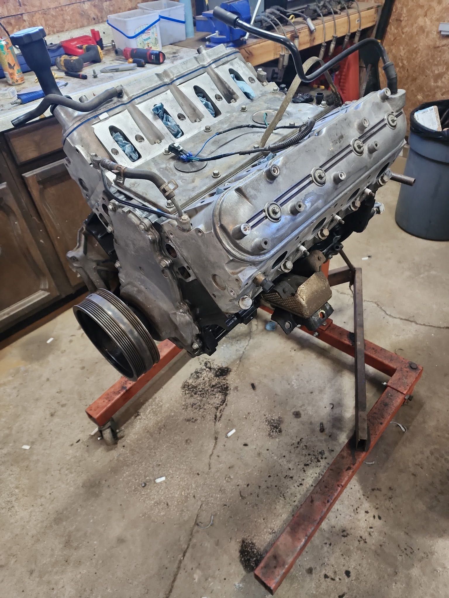 Engine block mounted on a red stand in a workshop, with tools and parts scattered nearby.