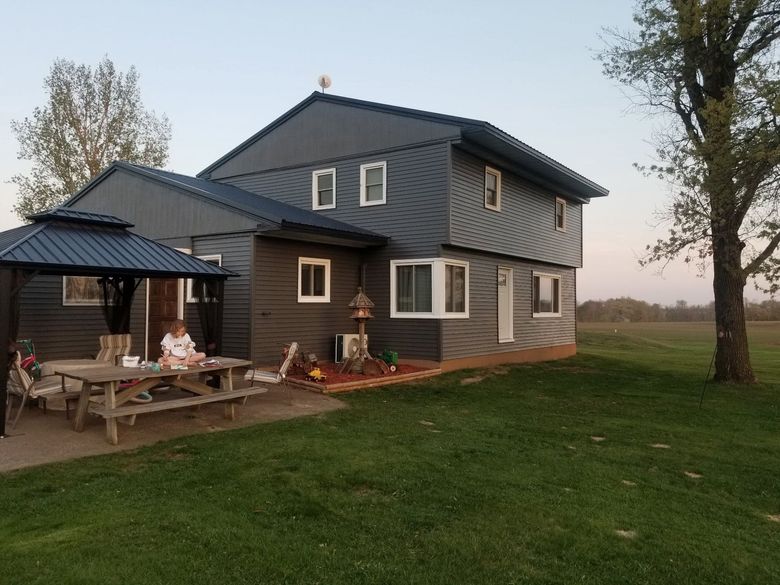 Modern gray two-story house with a small porch, picnic table, and campfire at dusk on a grassy yard