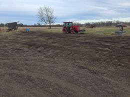 Red tractor working in a muddy field under a clear sky