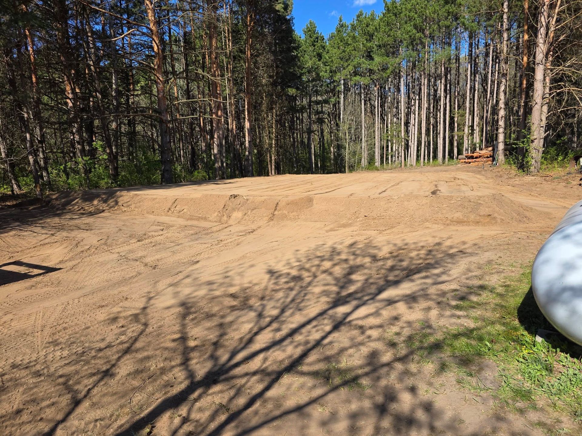 Dirt clearing in a wooded area under a clear blue sky, with trees surrounding the open space.