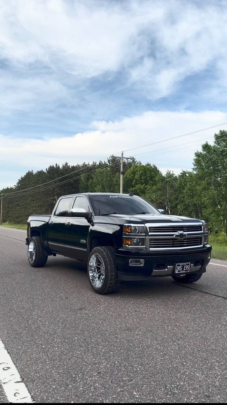Black lifted pickup truck parked on a gravel lot under a cloudy sky