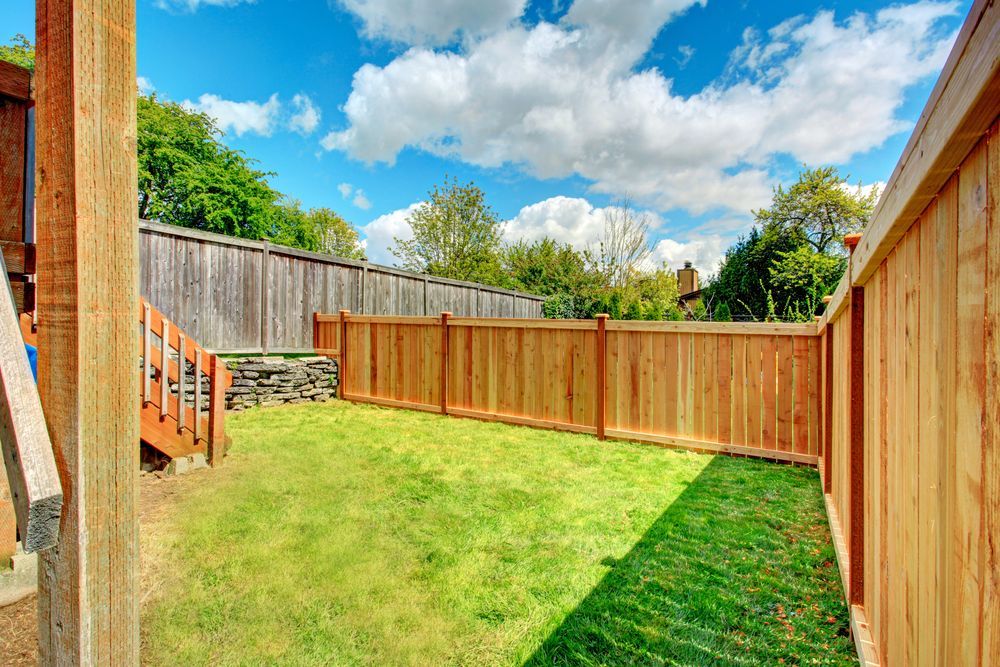 Small fenced backyard with green lawn, wooden deck steps, and blue sky with clouds