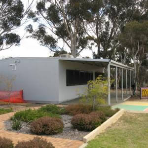 A white building with a covered porch and trees in the background.