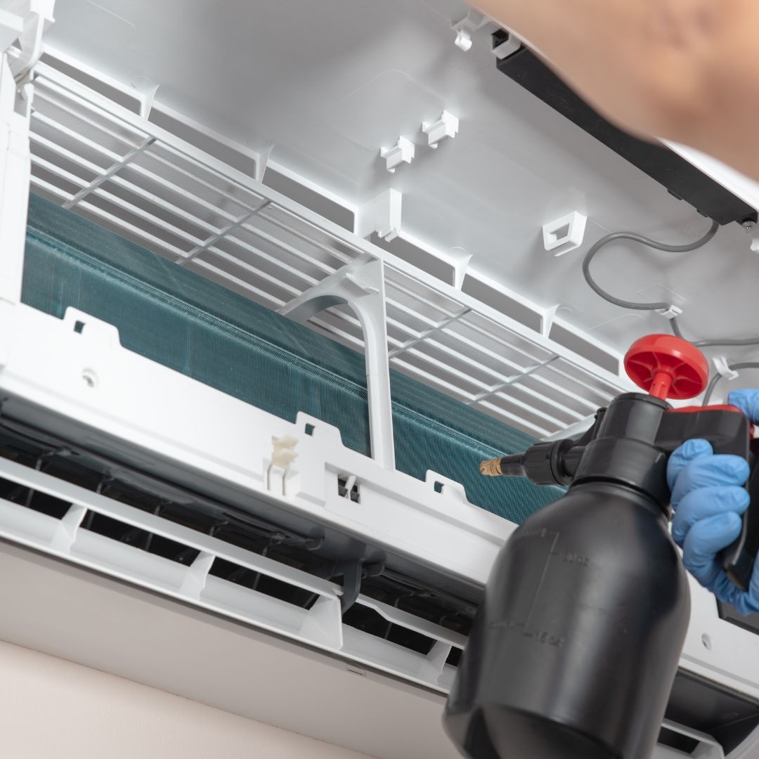 A person is cleaning an air conditioner with a spray bottle