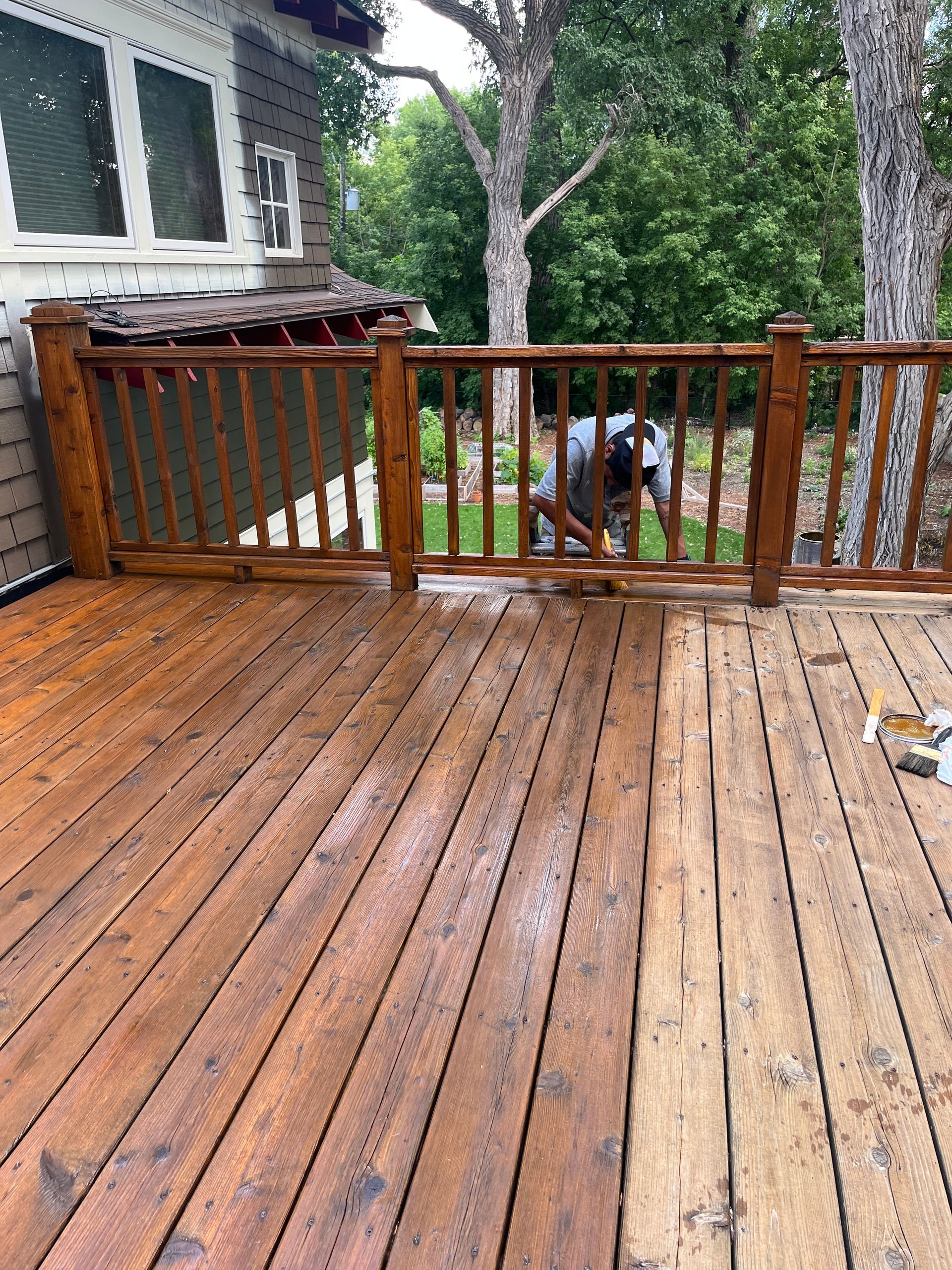 A man is cleaning a wooden deck in front of a house.