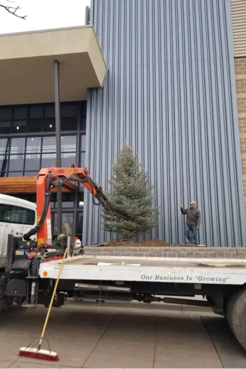 A tow truck with a broom attached to it is parked in front of a building.