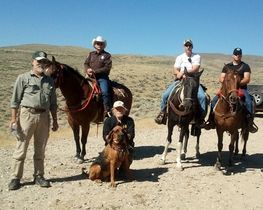 A group of people standing next to horses and a dog.