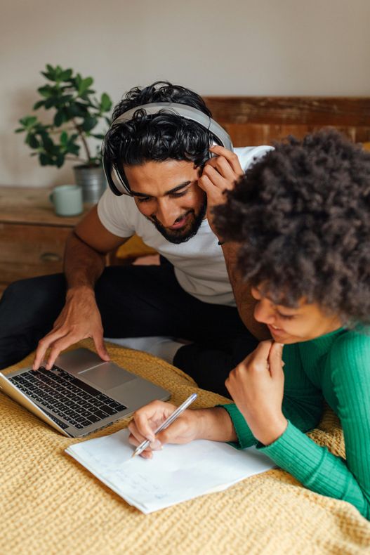 A man and a woman are sitting on a bed using a laptop computer.