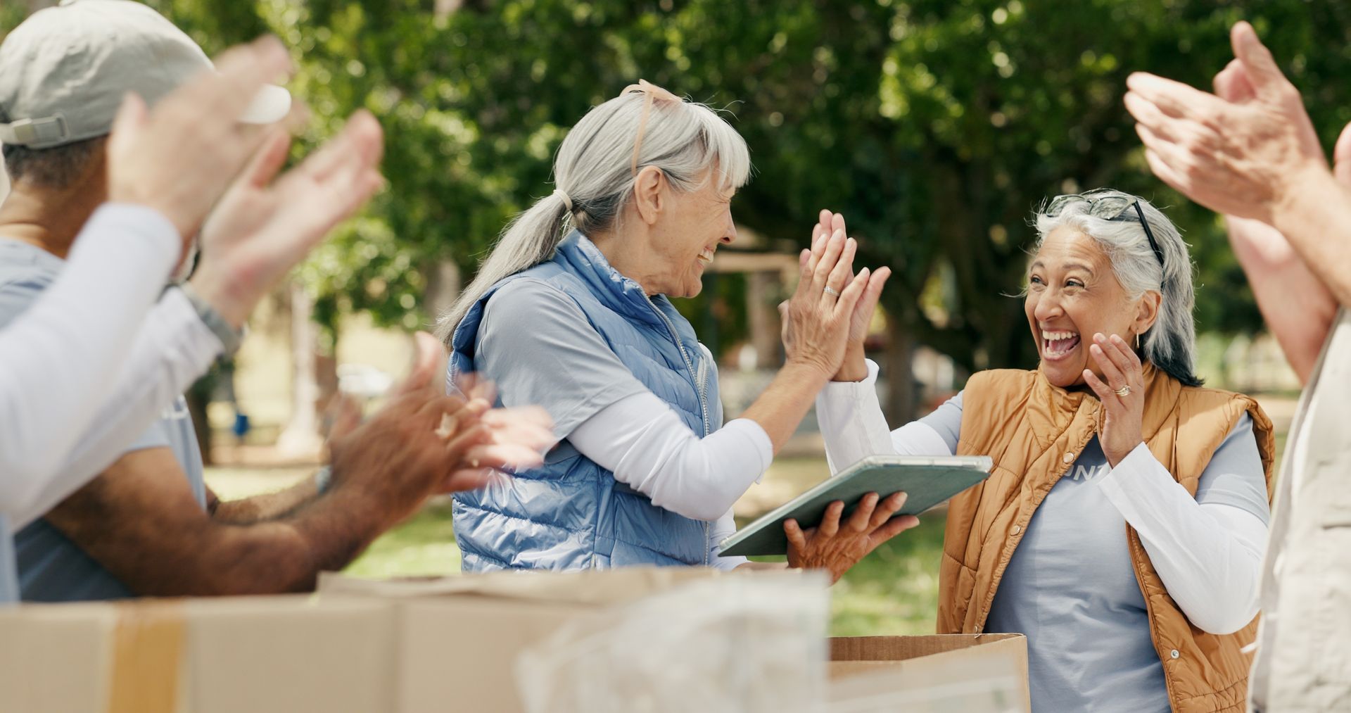 People sitting outdoors applauding and smiling during a lively gathering.