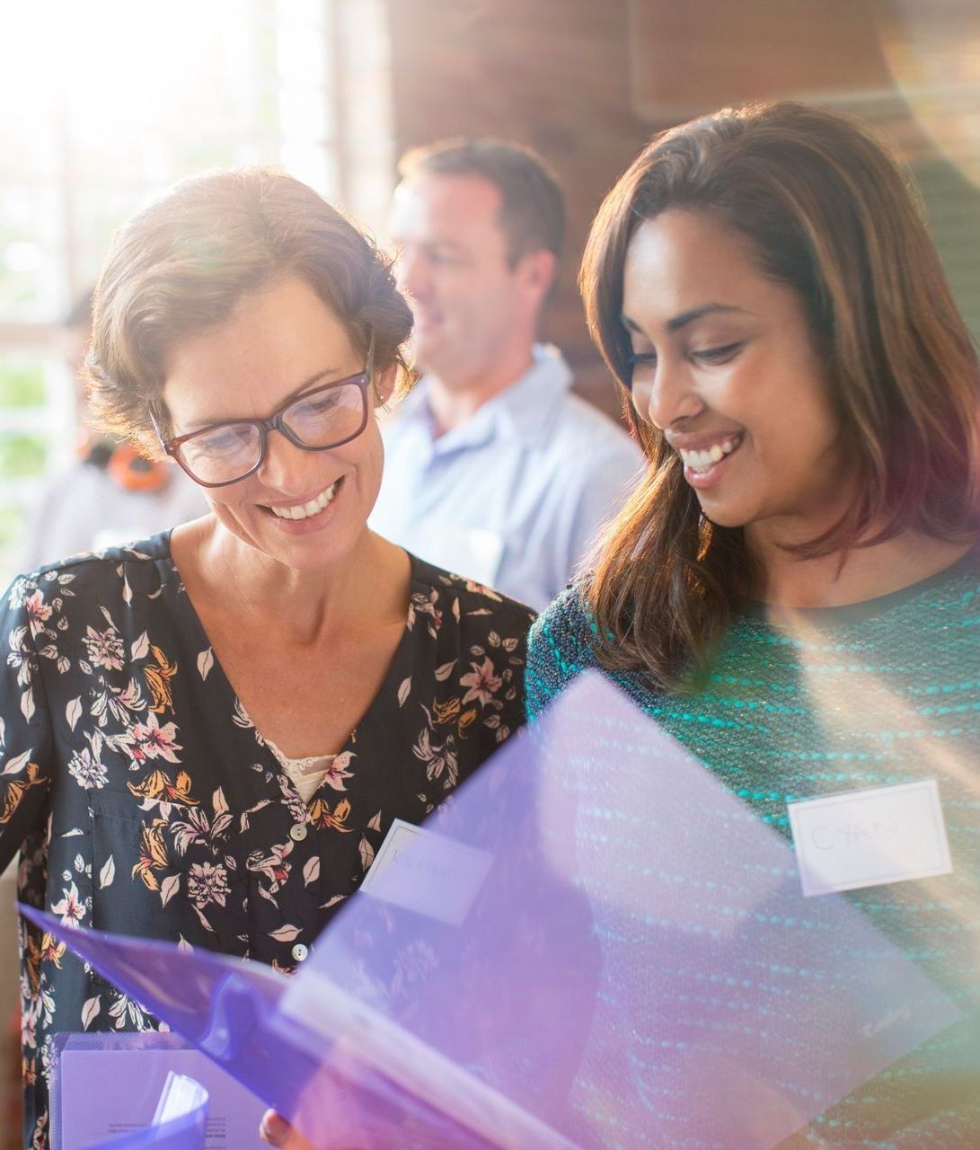 Two people smiling and looking at a purple brochure at a bright indoor event
