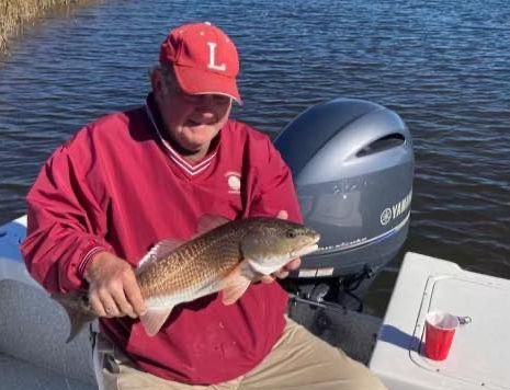 Angler in red cap and sweatshirt holds a fish on a boat beside an outboard motor.