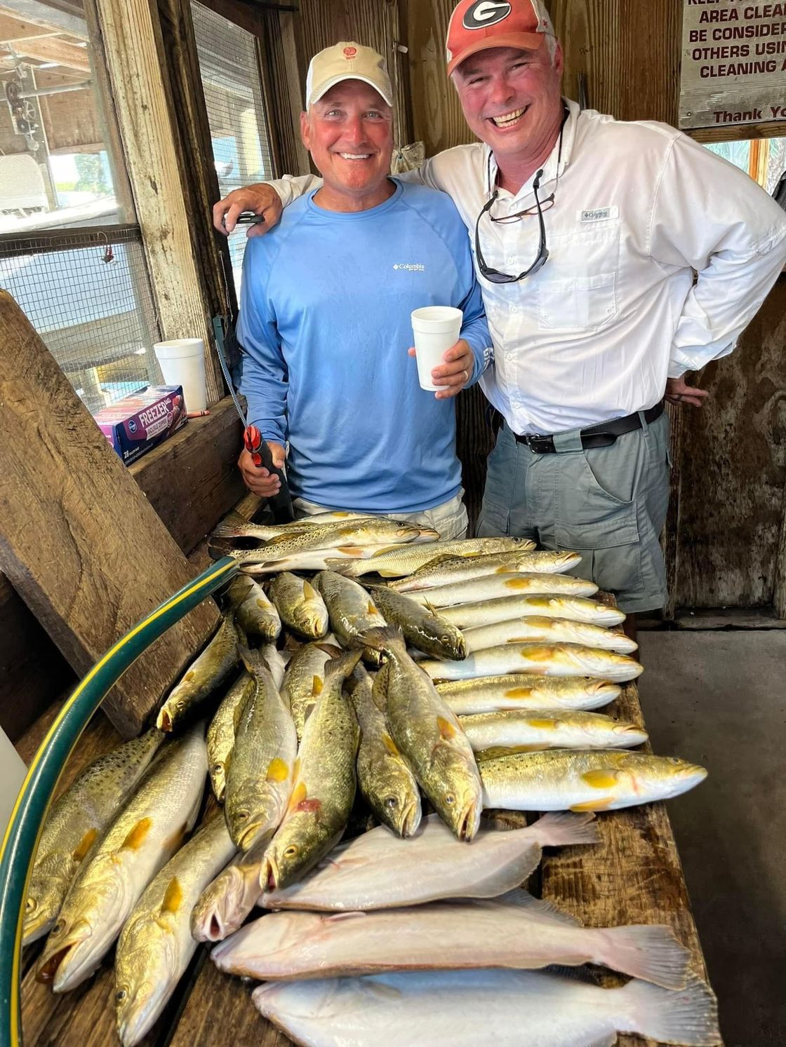 Two people smiling beside a table piled with fish at a dockside market