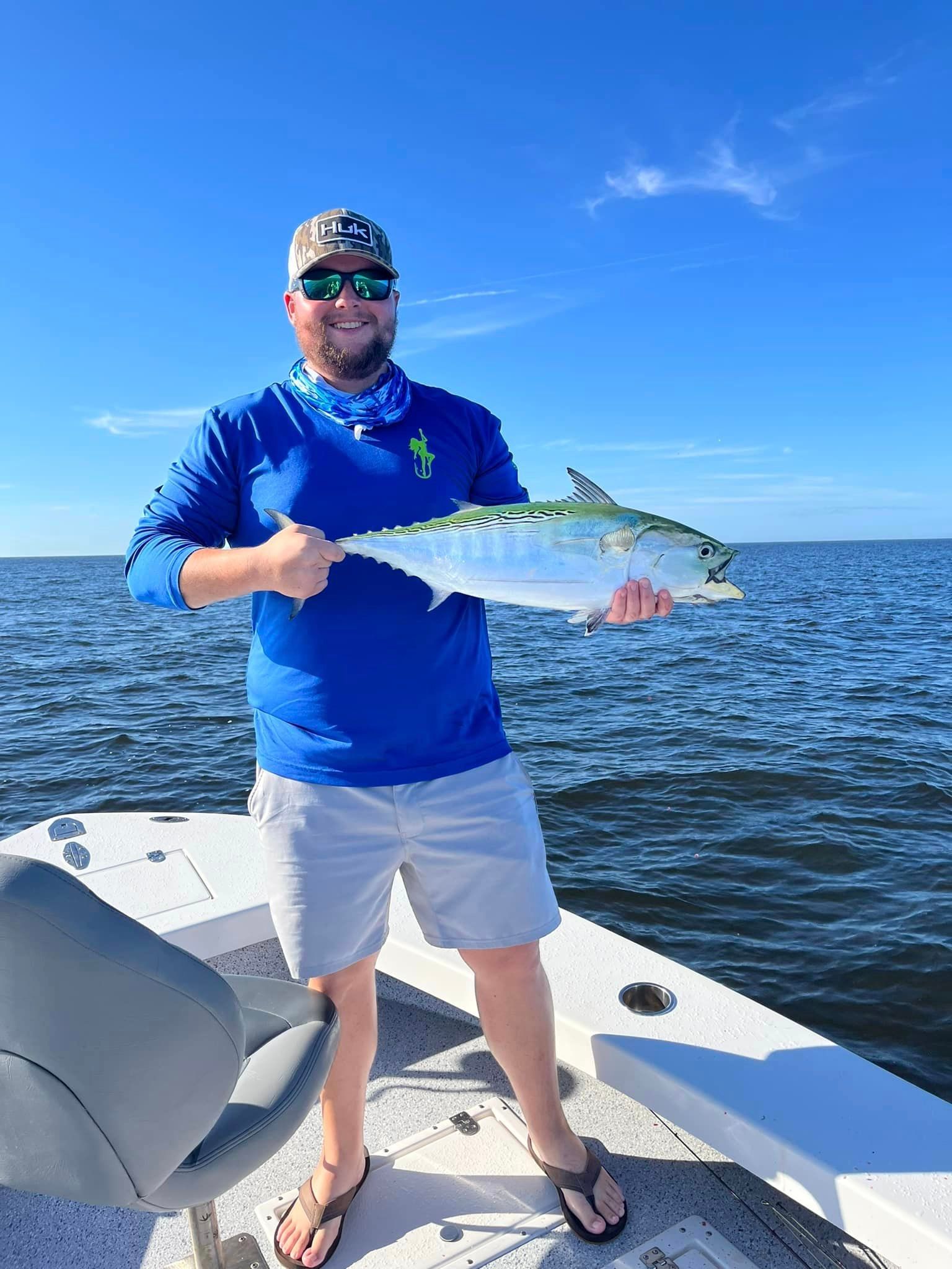 Angler on a boat holding a large silver fish on a sunny blue ocean
