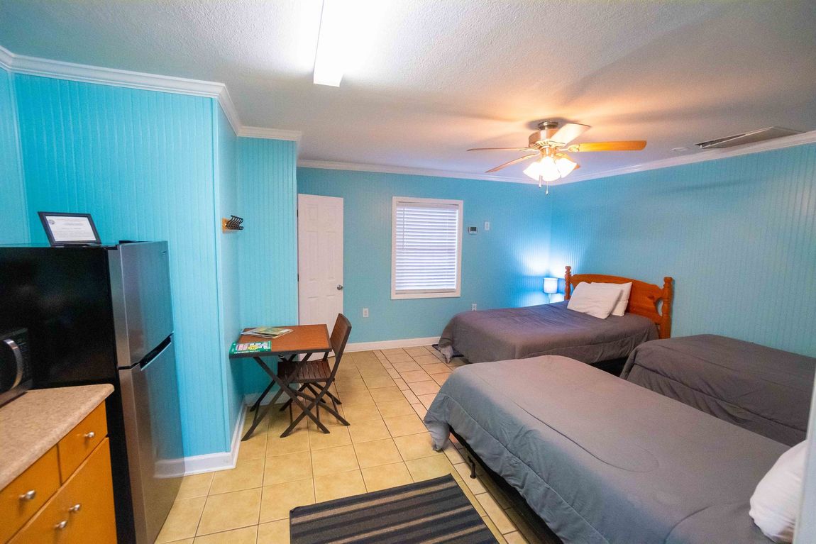 Bedroom with two beds, turquoise walls, a dresser, desk, and ceiling fan.