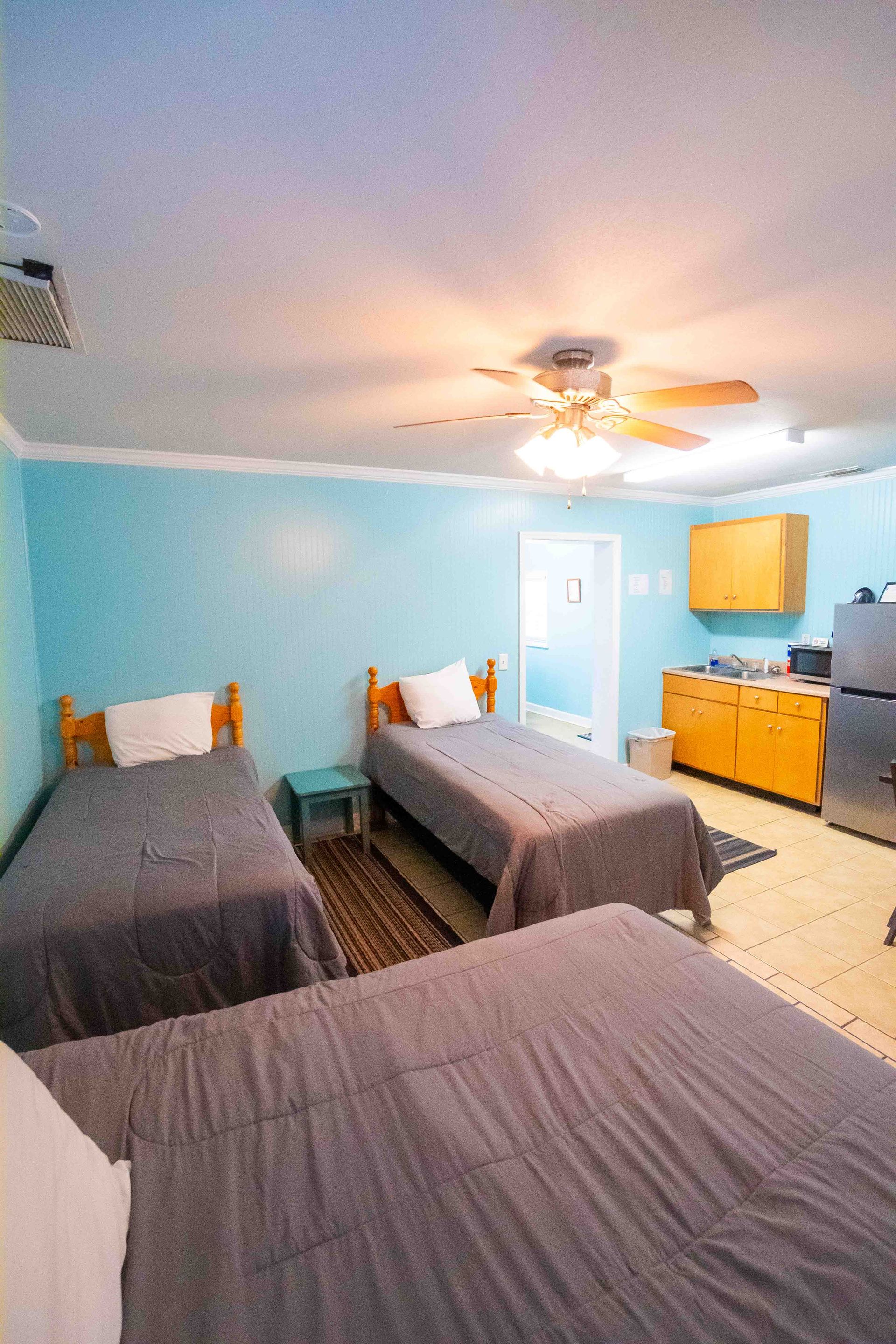 Bright bedroom with three twin beds, light blue walls, ceiling fan, and a dresser with mirror