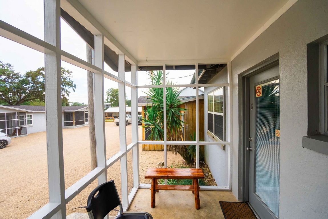 Covered porch with white railings, a small wooden bench, and a blue door beside a walkway.
