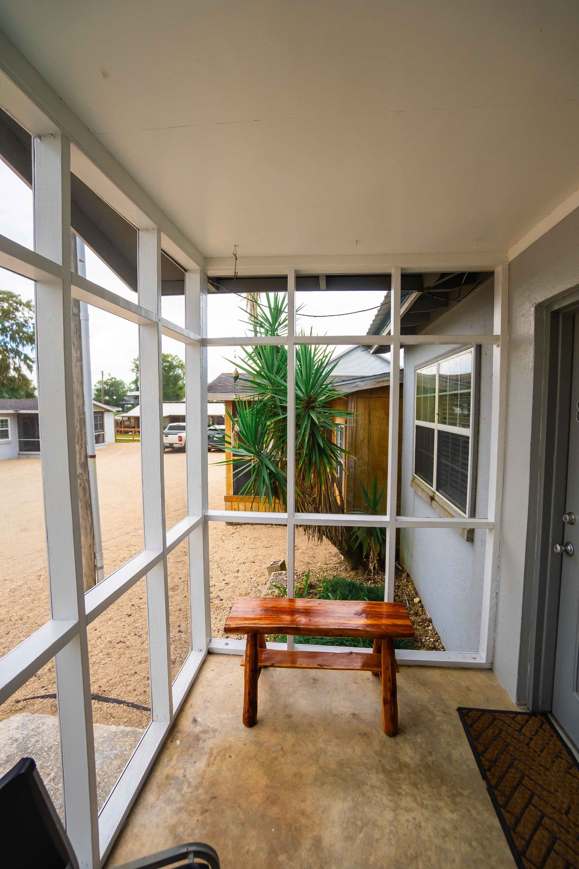 Covered porch with a wooden bench, white railing, and a view of a yard and potted plant outside.