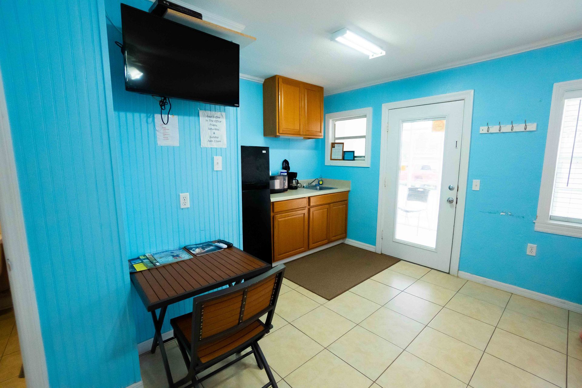 Small waiting room with blue walls, TV, desk, chairs, cabinets, and a door to the outside.