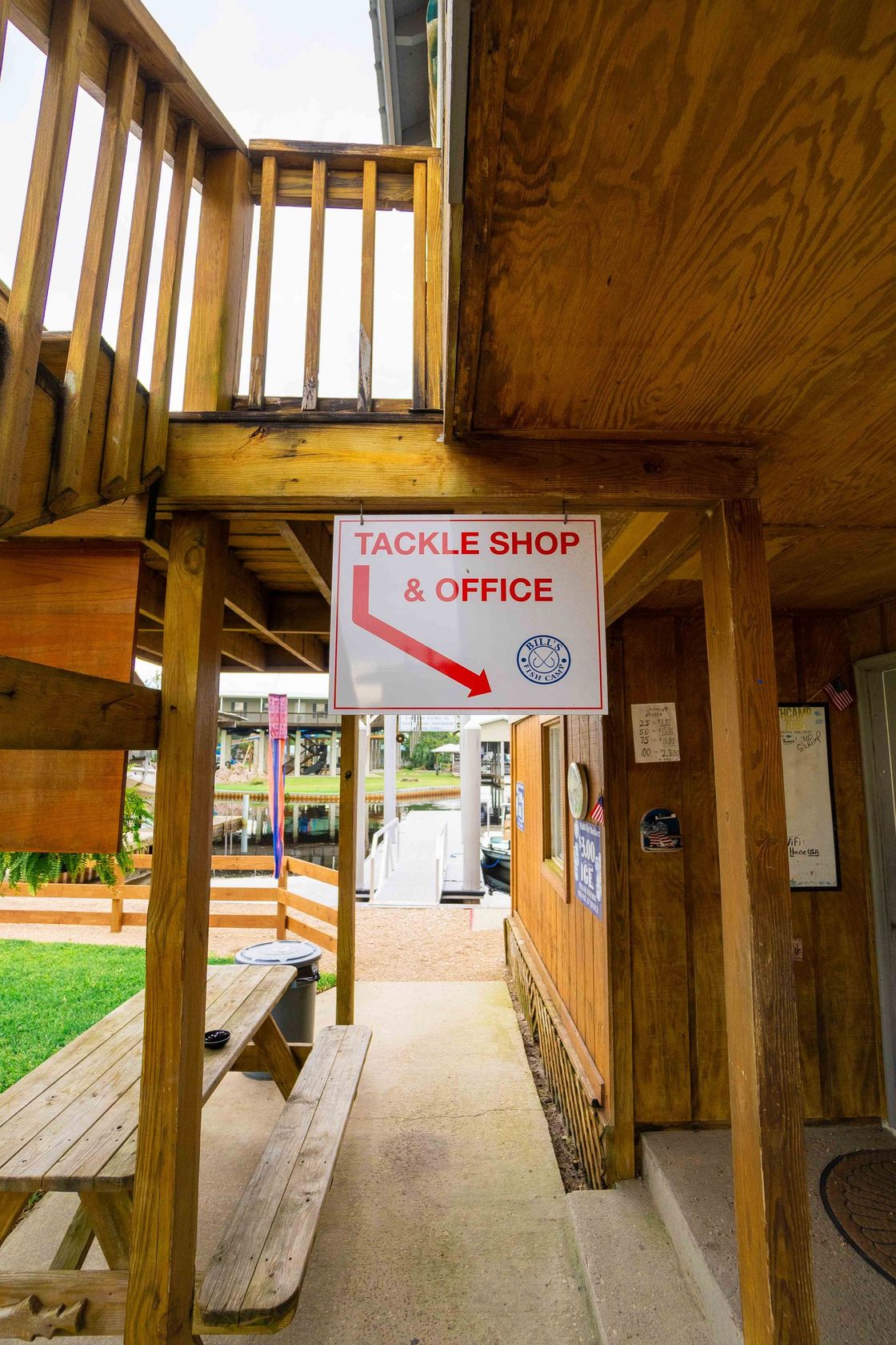 Wooden lodge walkway with a hanging sign reading “Tackle Shop & Office” and a red arrow pointing down.