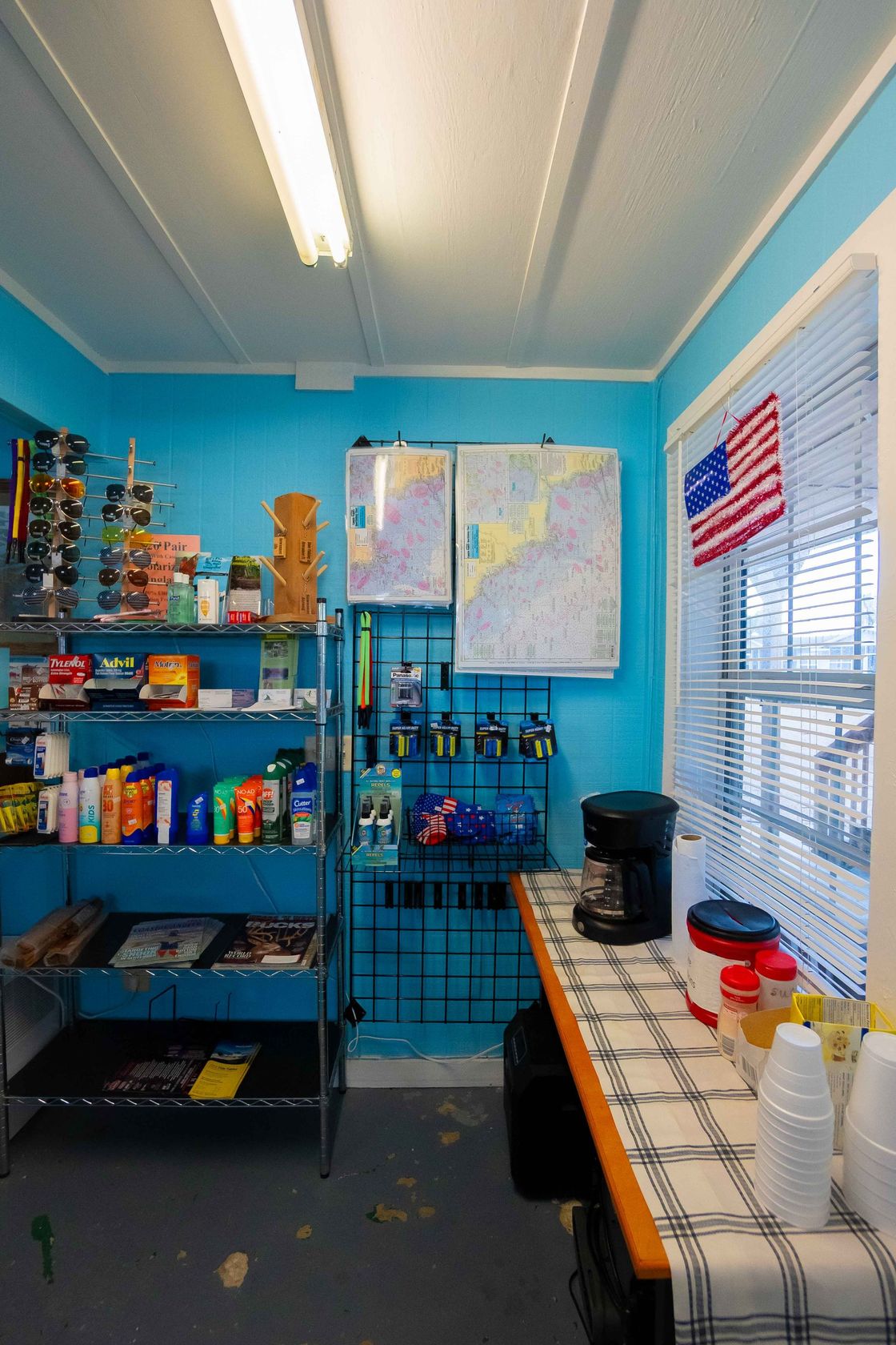 Small blue workshop with shelves of supplies, a window with blinds, and a table holding bottles and jars.