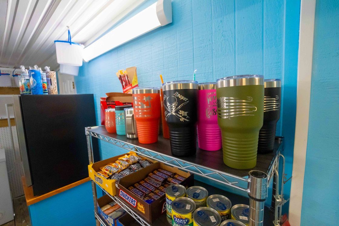 Colorful cups and canned drinks displayed on a metal shelf against a blue wall in a store.