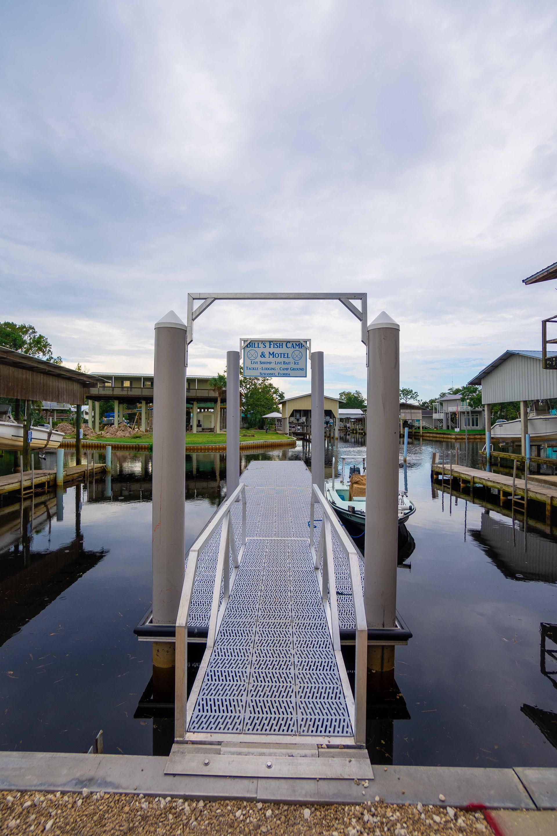 Marina dock with white walkway and overhead arch over calm water under a cloudy sky