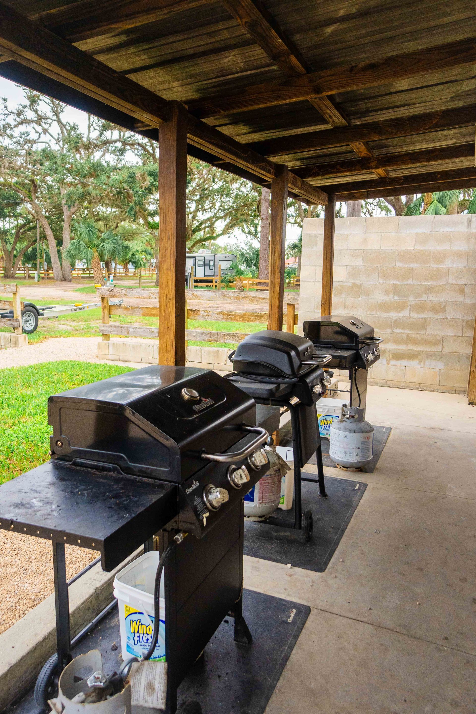 Covered outdoor grill area with three black barbecue grills on a concrete patio