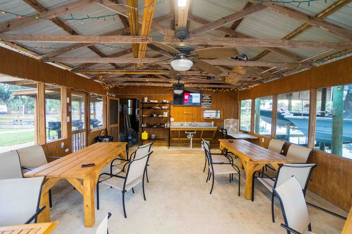 Open-air wooden patio with tables and chairs, serving counter, and windows overlooking the water.