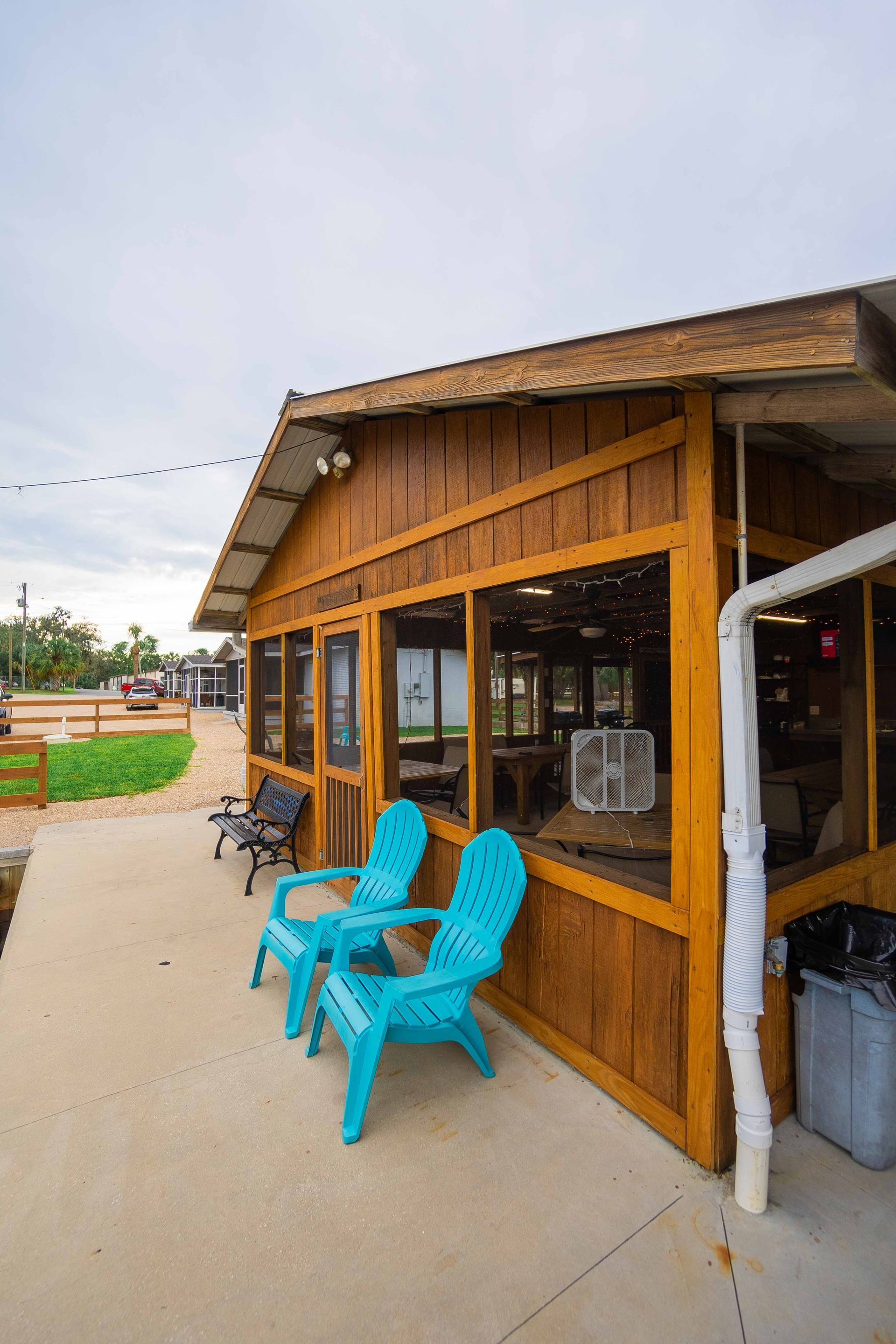 Small wooden café with bright blue chairs outside on a concrete patio.