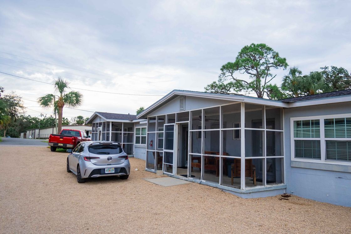 Modern single-story home with screened porch, parked cars, and gravel driveway under a cloudy sky