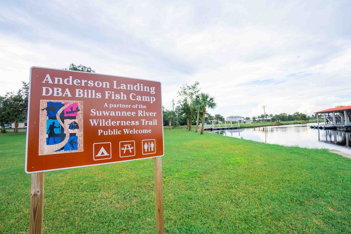 Sign for Anderson Landing on a grassy riverbank beside a calm waterfront.