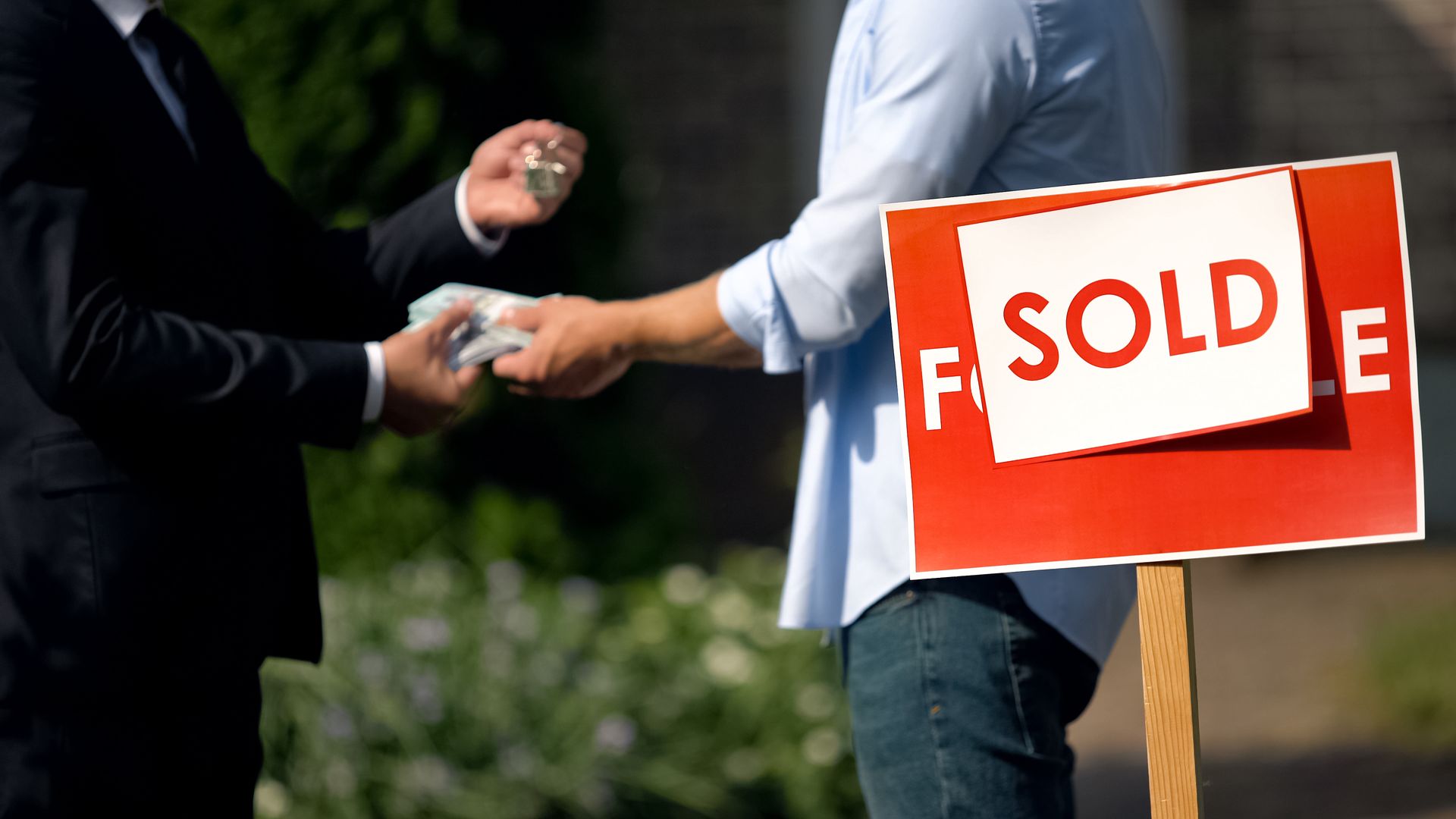 The agent and buyer swap cash and house keys beside a bright SOLD sign.