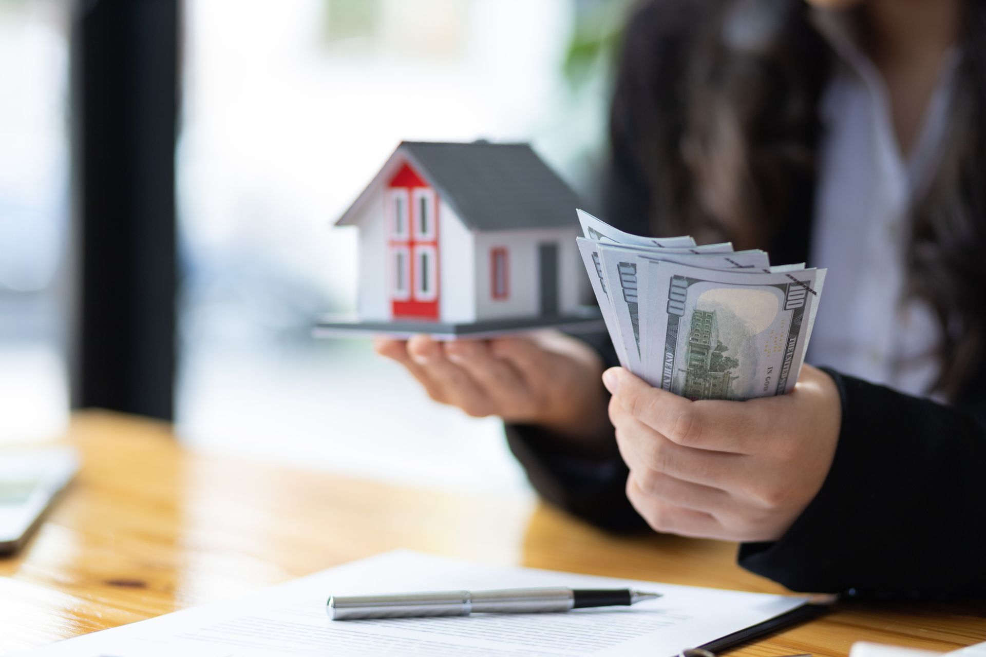 Home buyer holding cash and a mock-up home in her office.