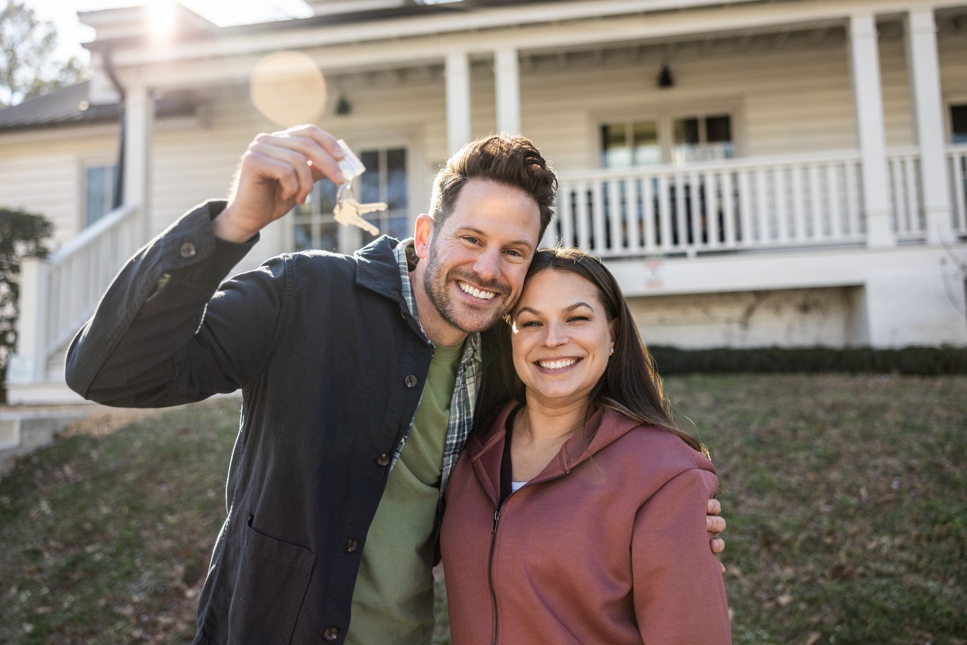 Excited home buyers celebrating with house keys in front of their new home.