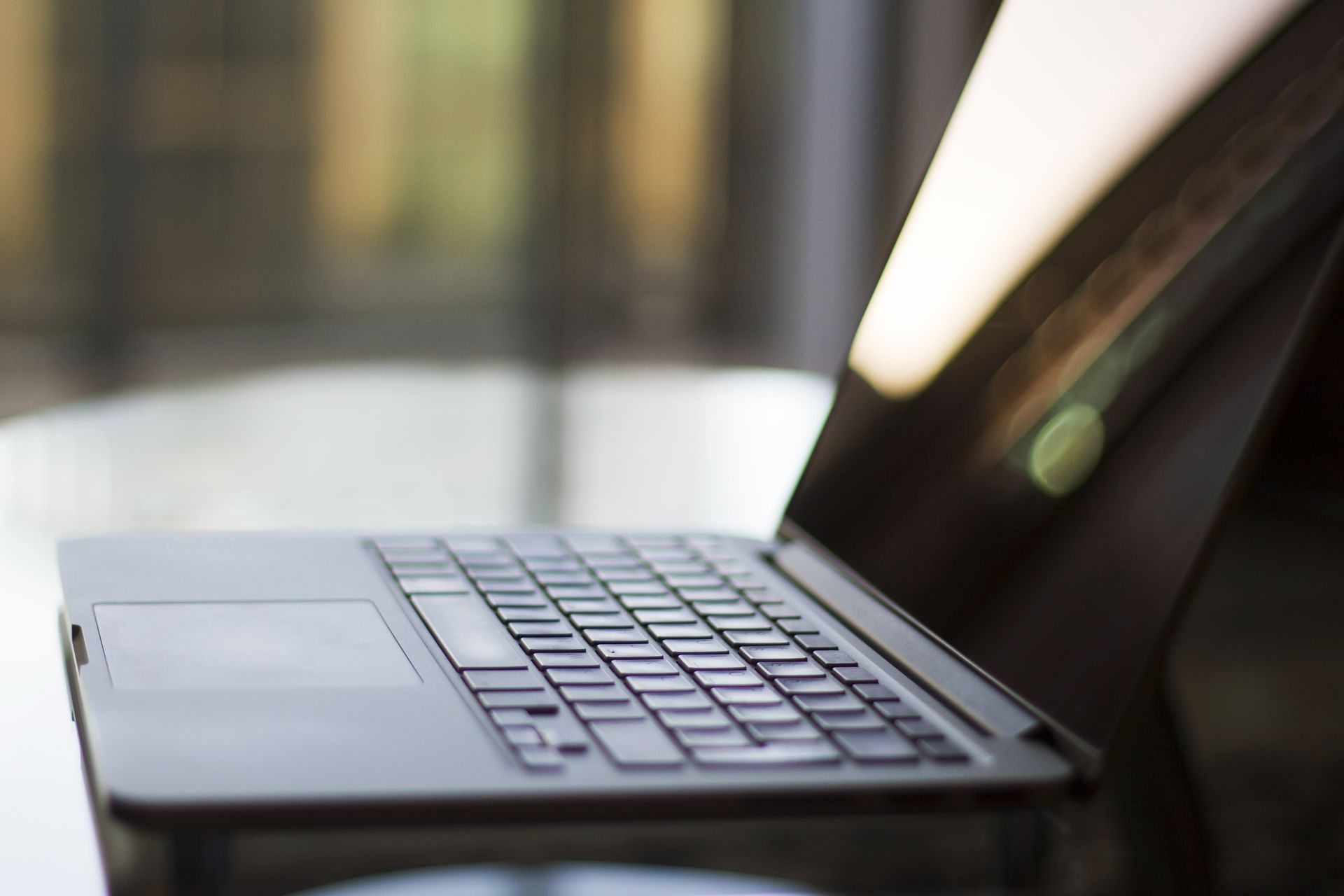 Laptop with a dark keyboard, open on a reflective surface, blurred background with natural light.
