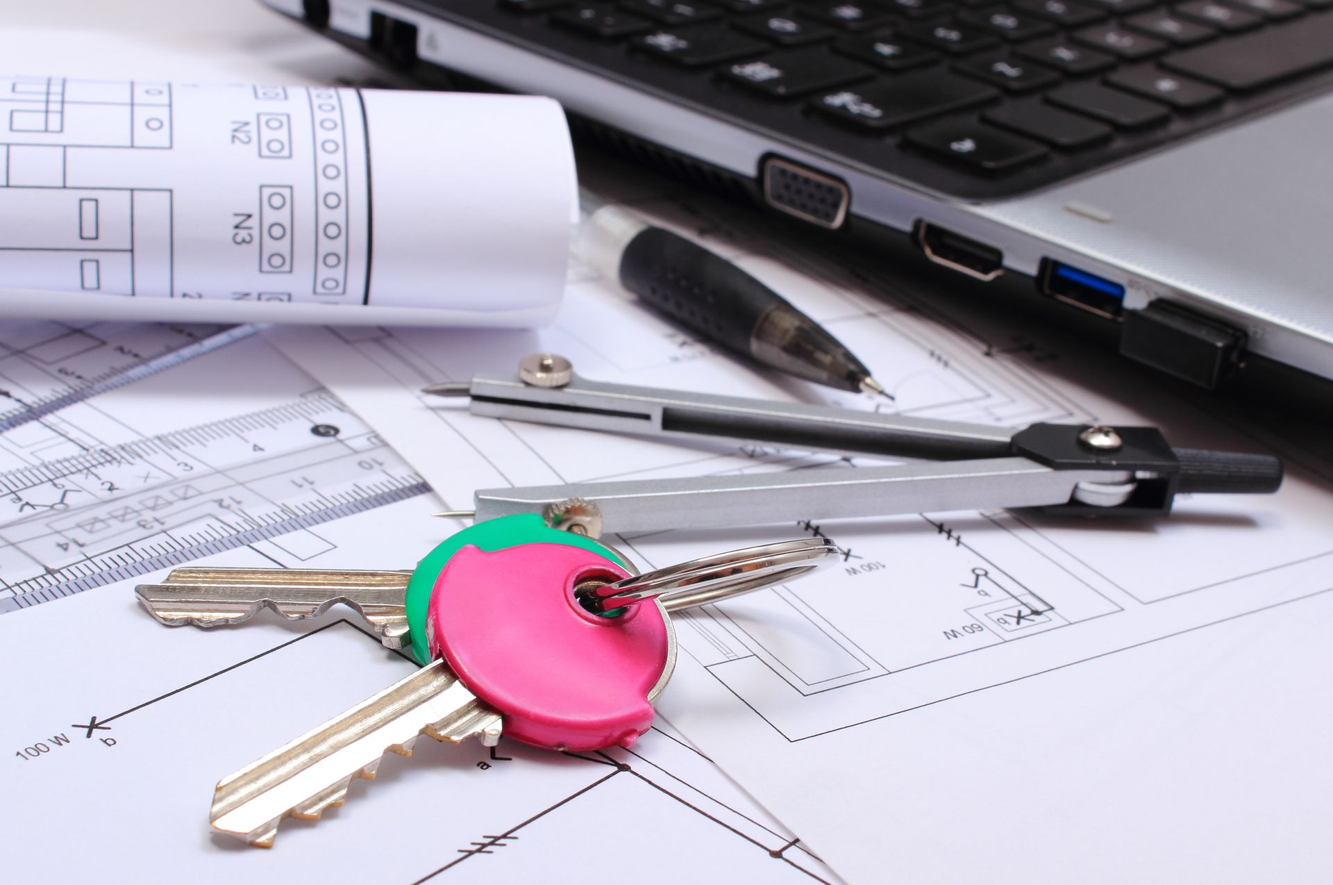 Keys on blueprints with laptop, drafting tools, and rolled architectural plans.