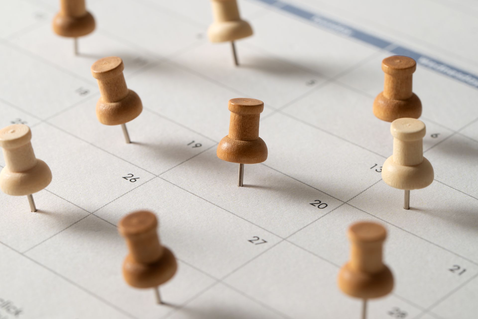Calendar page with multiple wooden pushpins marking dates.