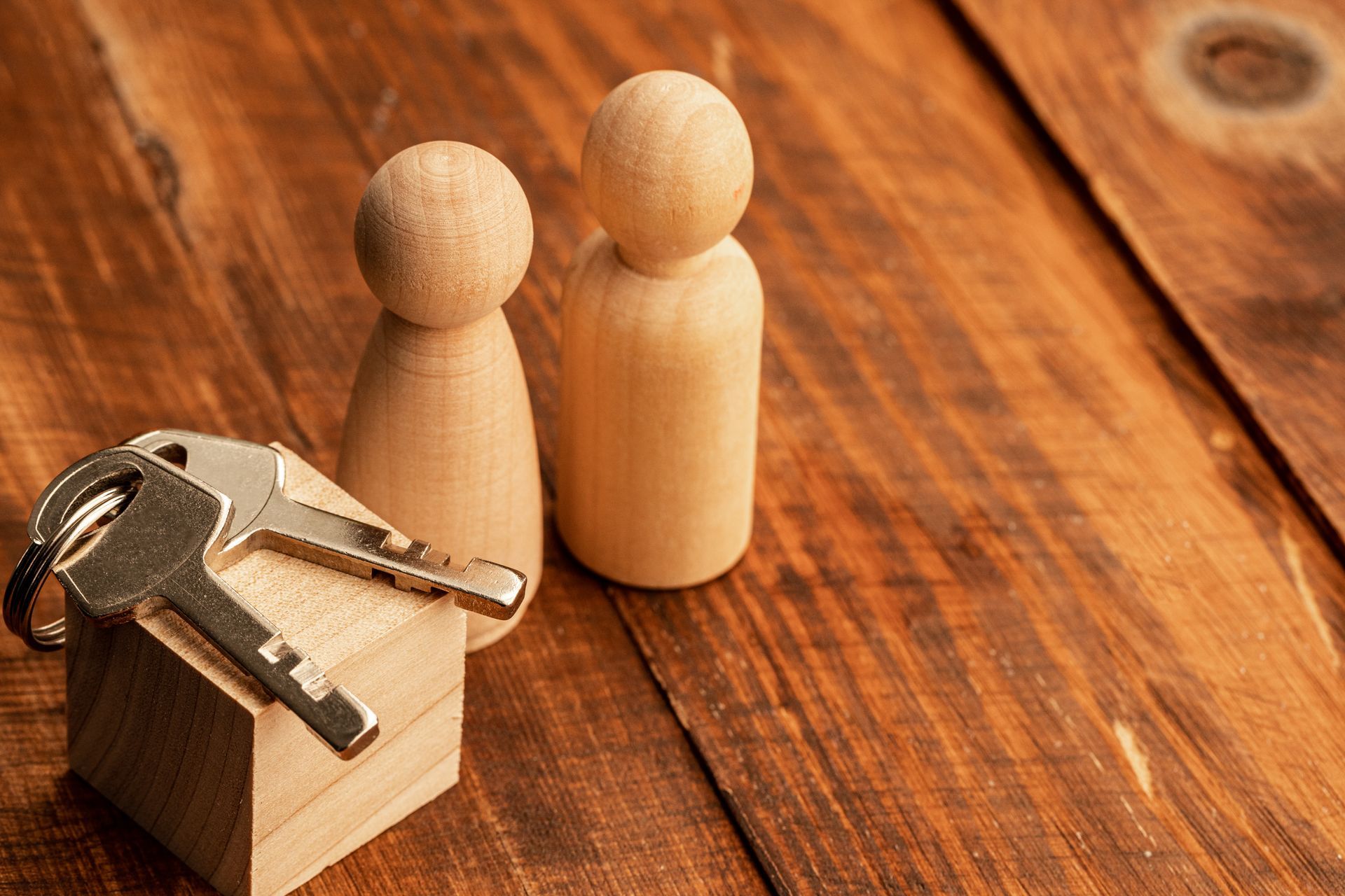 Wooden figures and house model with keys on a wooden table, symbolizing homeownership.