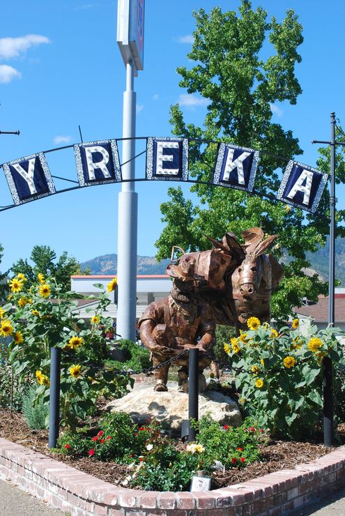 Flower bed with animal sculptures and “YREKA” sign under a blue sky