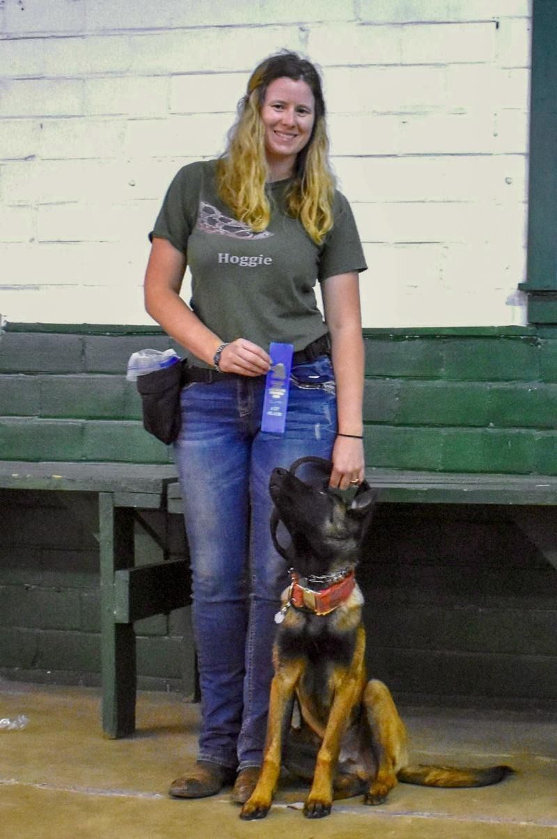 Woman standing beside a seated German shepherd indoors