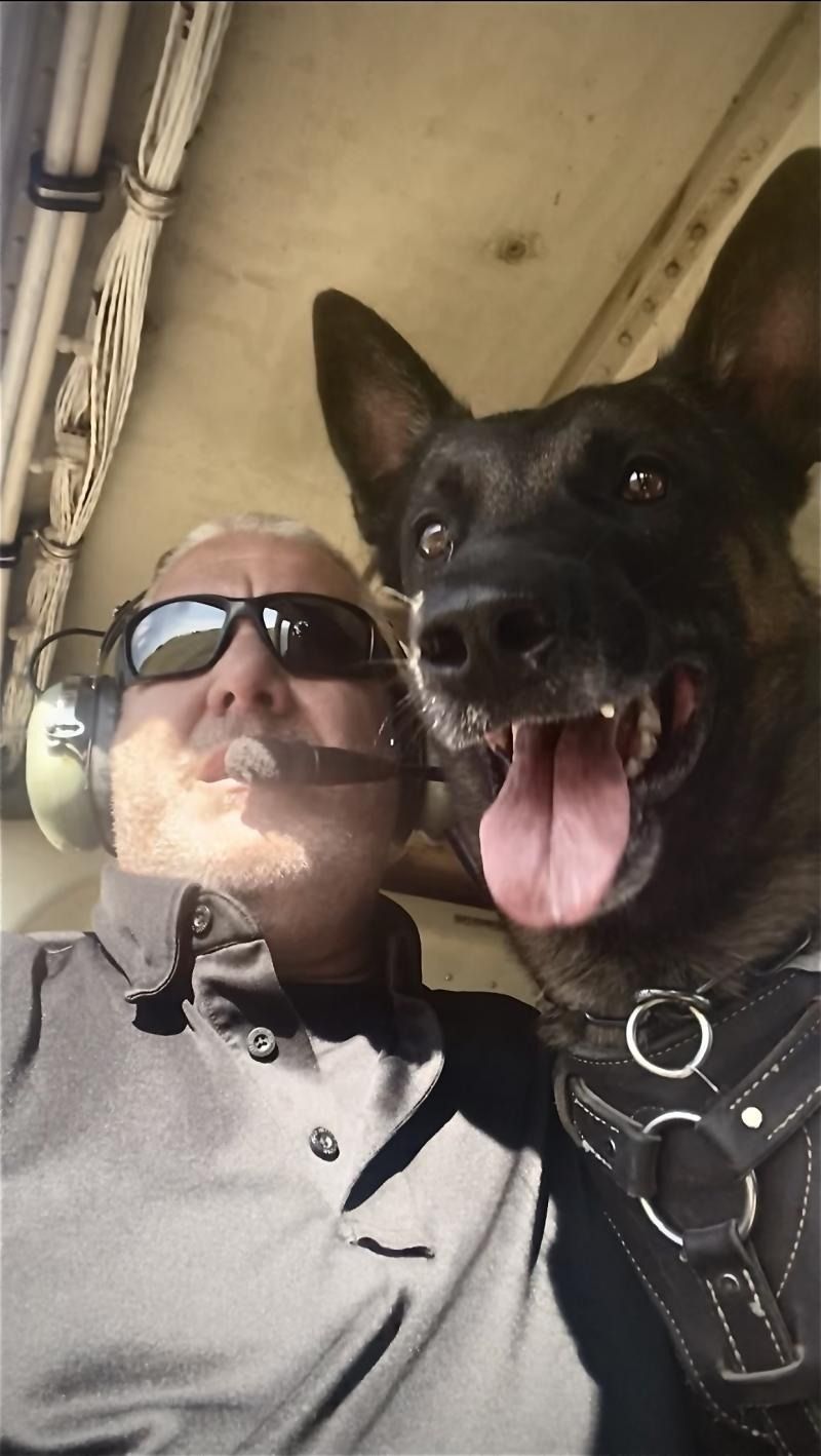 Man wearing sunglasses and headphones taking a selfie with a panting German shepherd in a vehicle