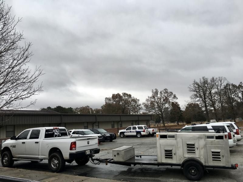 Parking lot with several vehicles and a white utility trailer under a cloudy sky